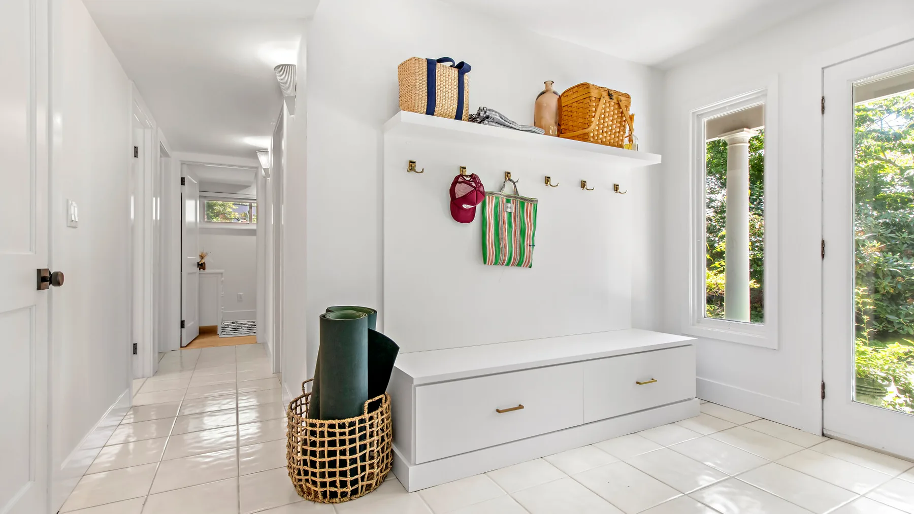 A bright entry hall has a built-in bench, wall hooks, and a glass door.
