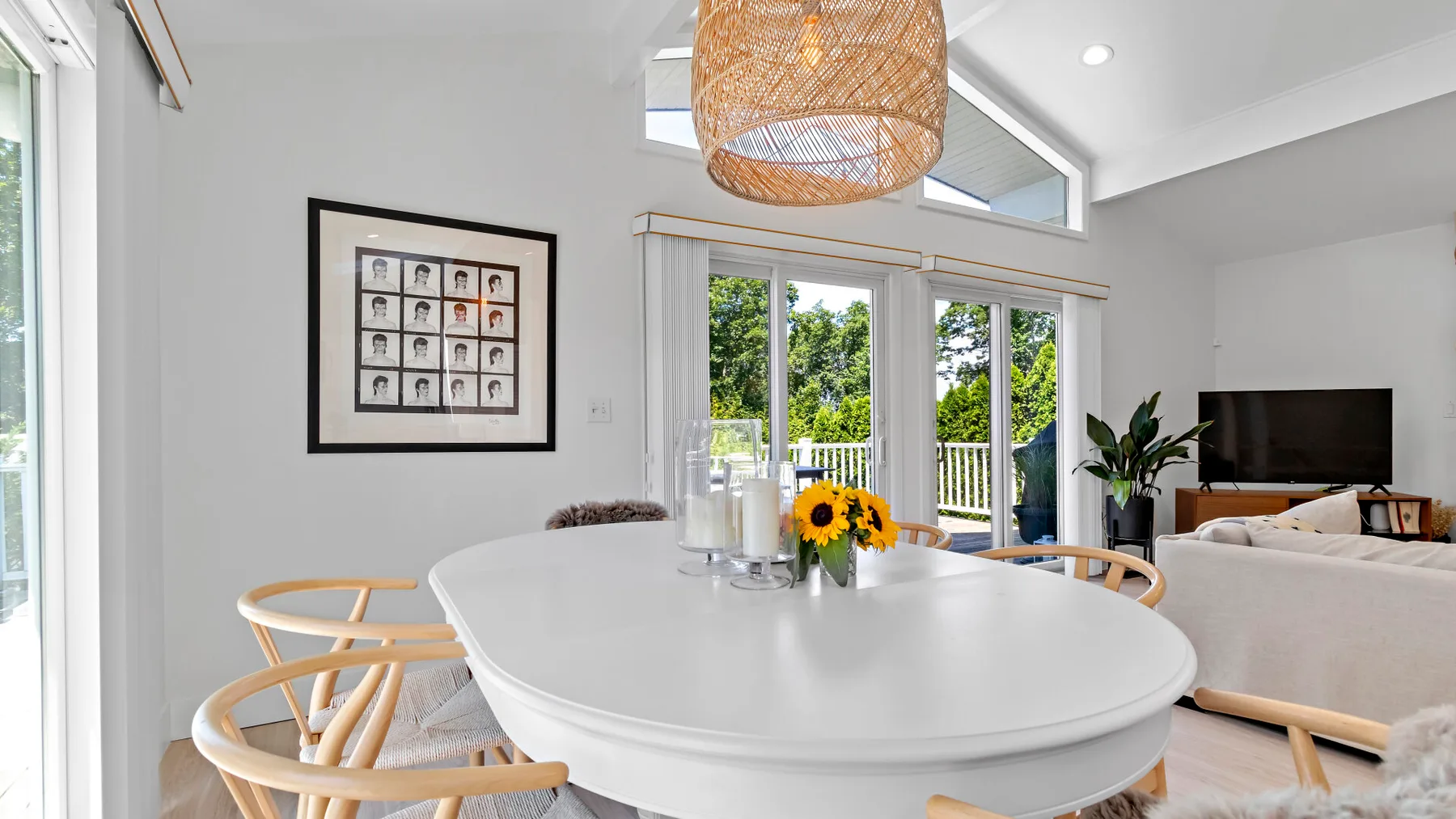 A bright dining area with a white table, woven chairs, and windows overlooking greenery.