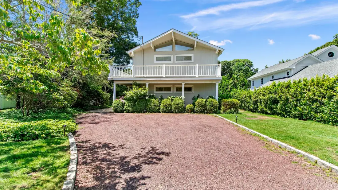 A two-story house with a balcony stands beyond a broad gravel driveway.