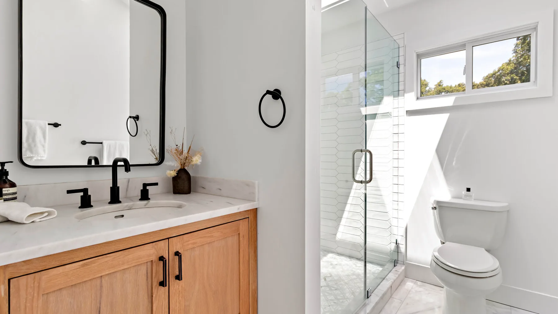 A bright bathroom with a wood vanity, sink, glass shower, and toilet.