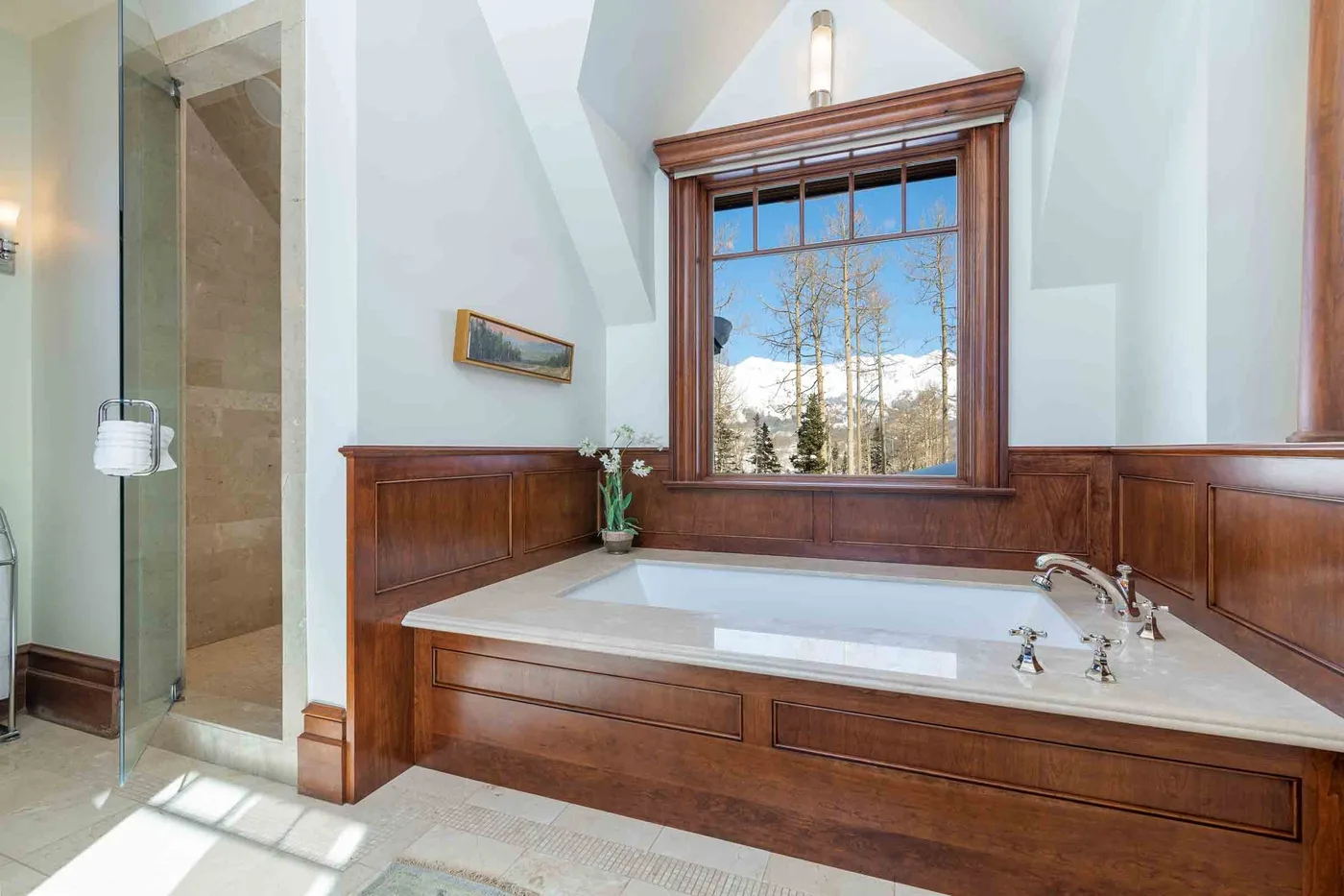 A built-in bathtub sits beneath a large window in a wood-paneled bathroom.