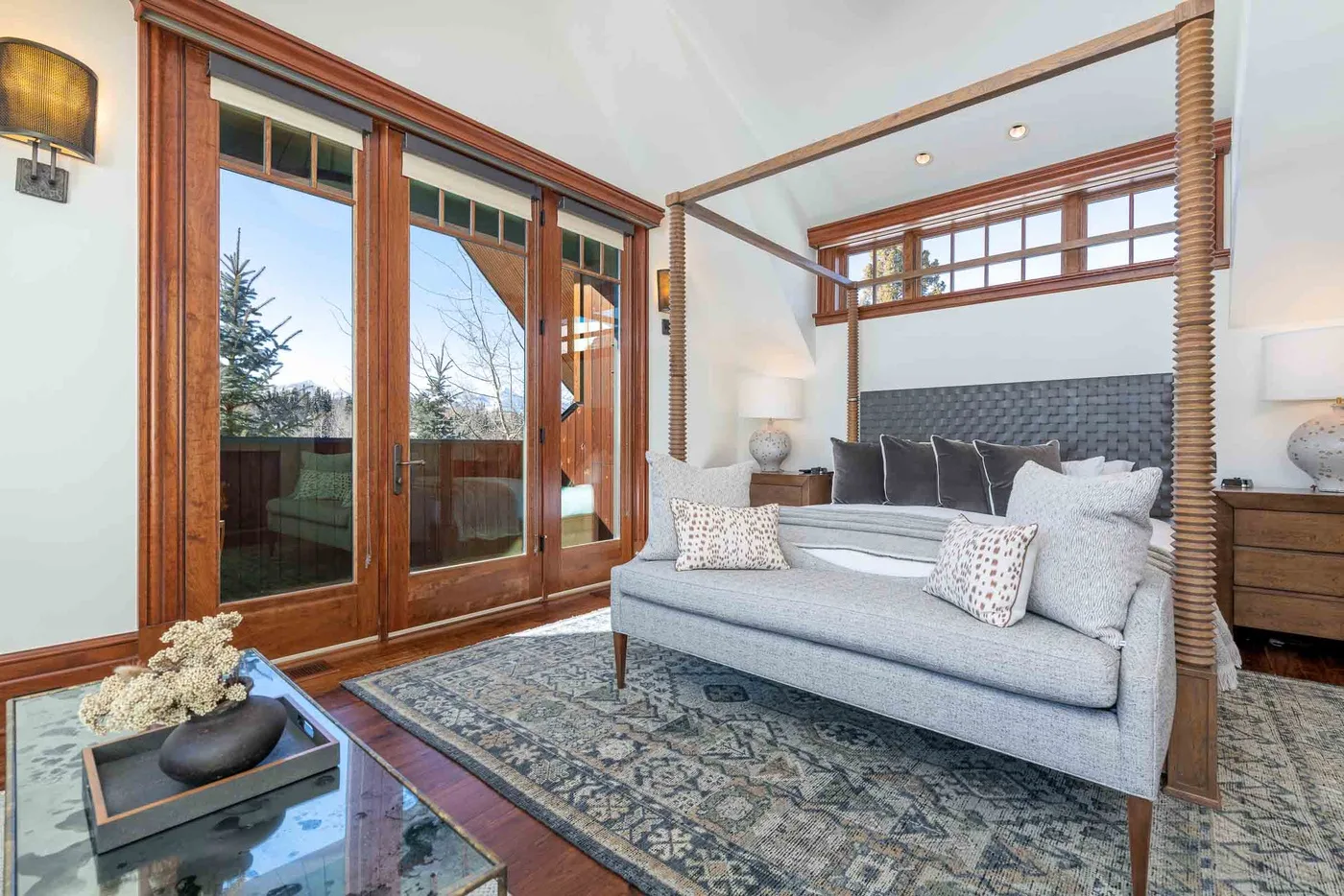 A bright bedroom with a bed beside tall wood-framed glass doors.