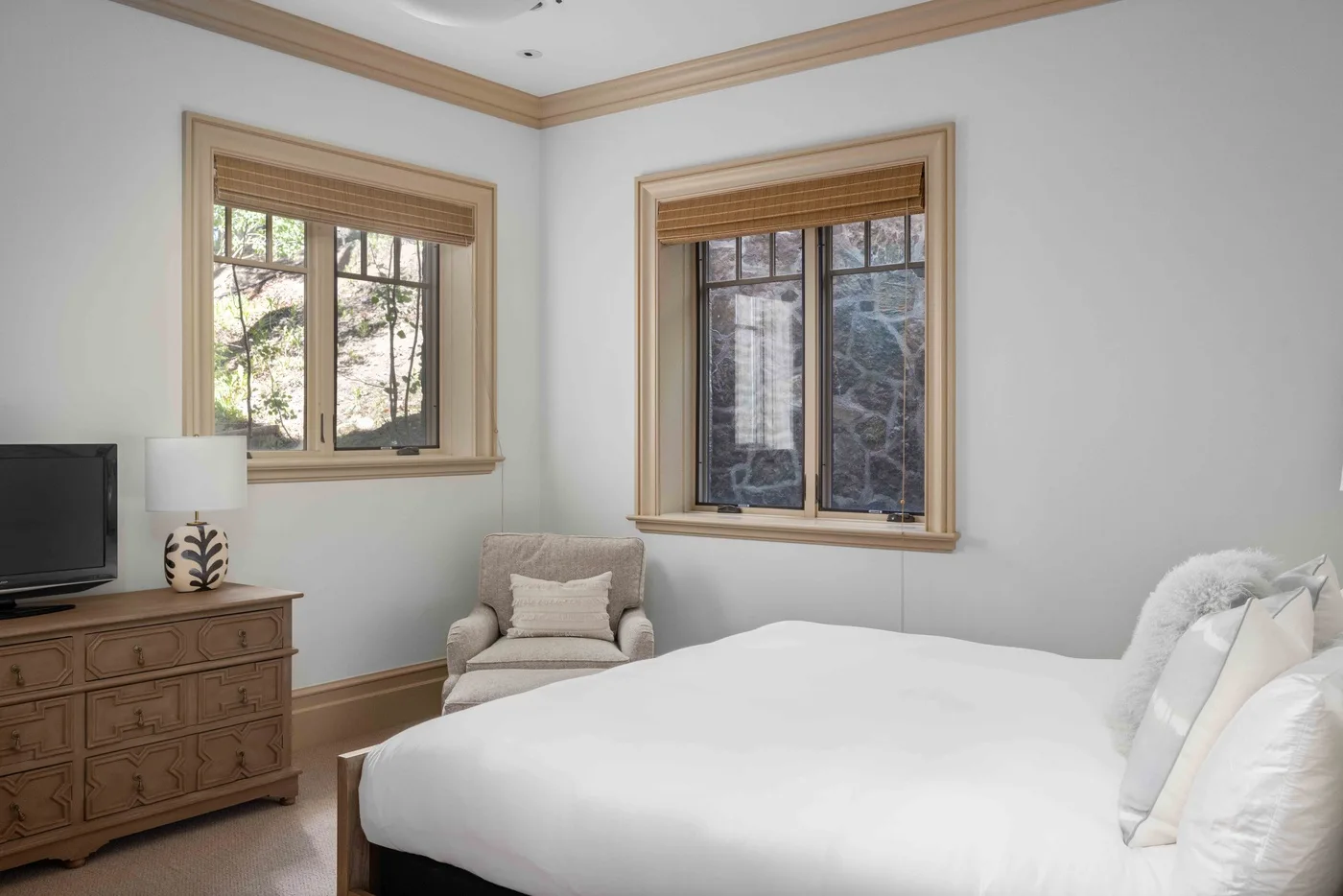 A bedroom with a large bed, an armchair, and two windows.