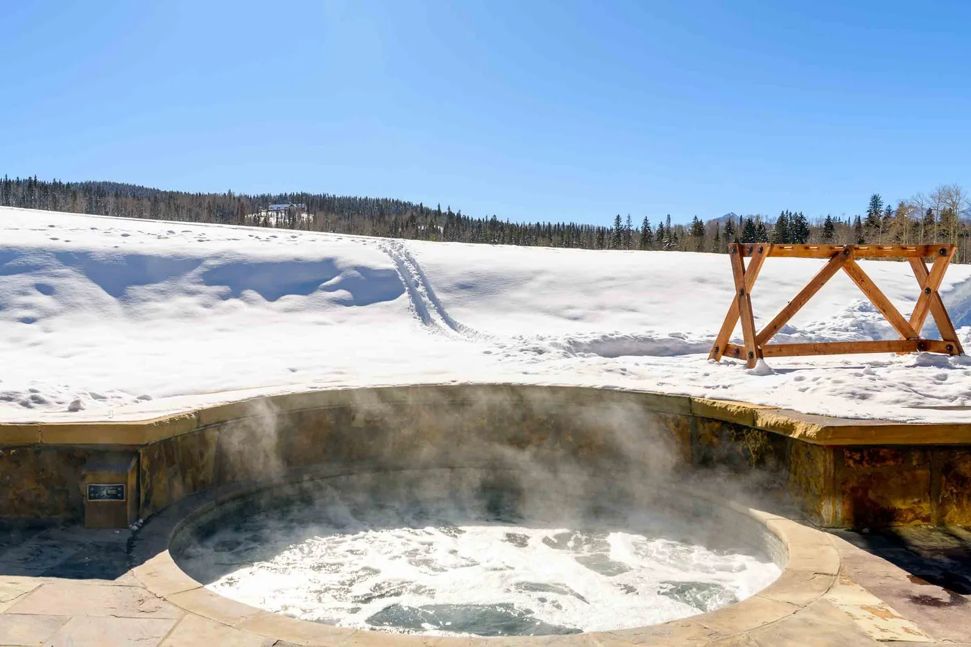 An outdoor hot tub steams beside a snowy field under a clear sky.