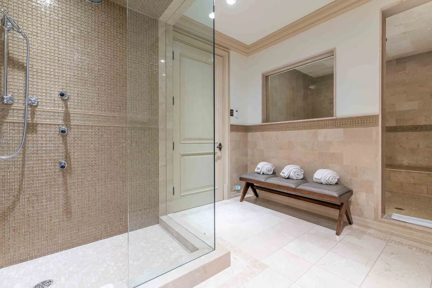 A tiled bathroom with a glass shower and a bench along the wall.