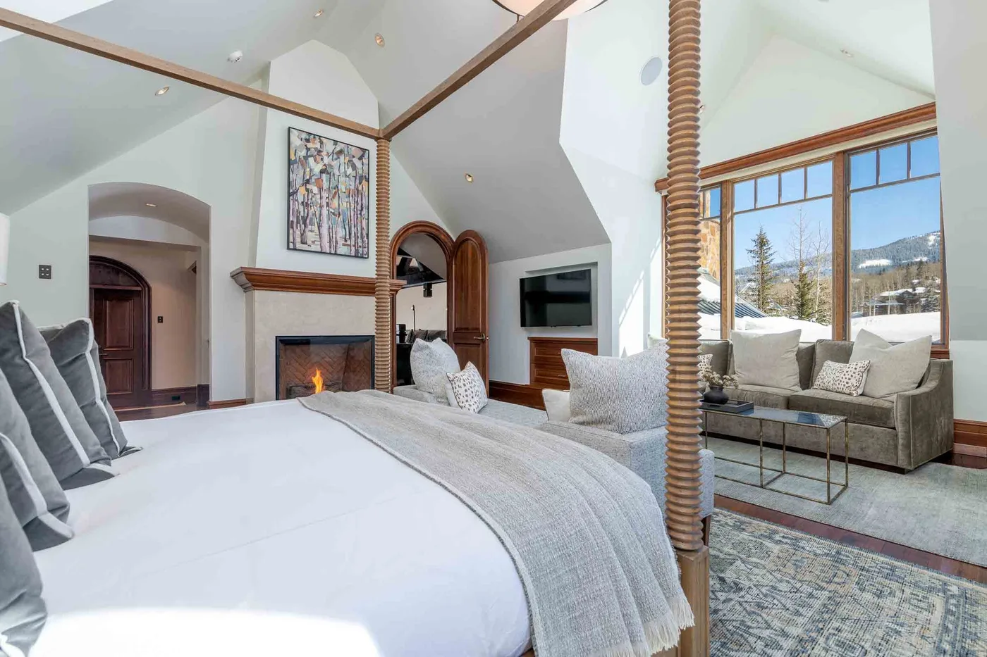 A bedroom with a large bed opens onto a sitting area by tall windows.