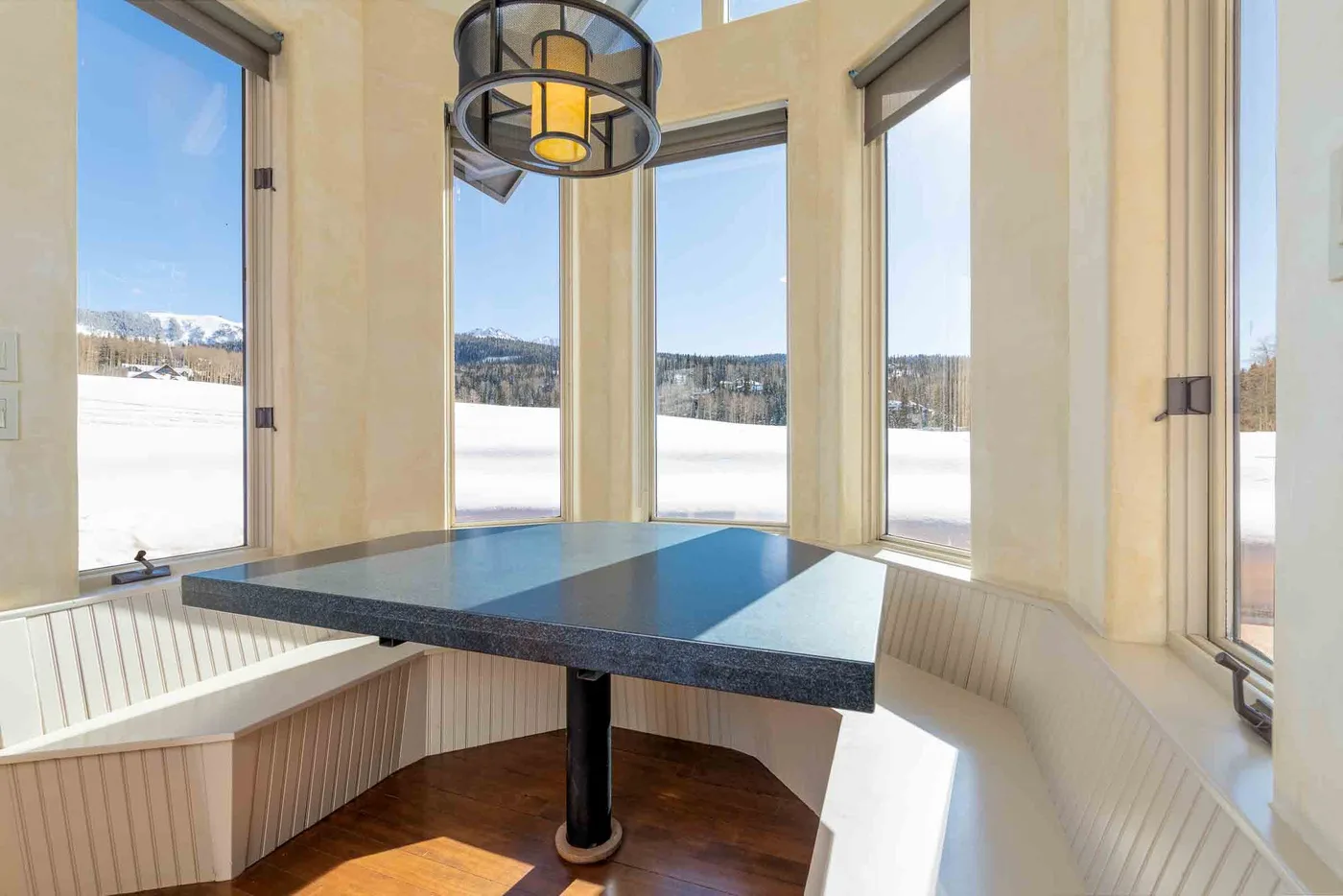 A bright dining nook with a dark table beside large windows overlooking a snowy landscape.