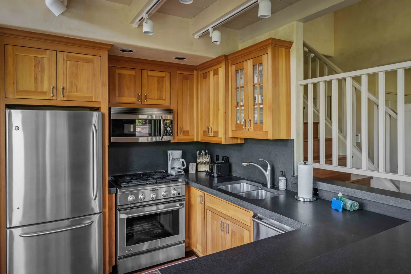 A kitchen with wood cabinets, stainless steel appliances, and a dark countertop.