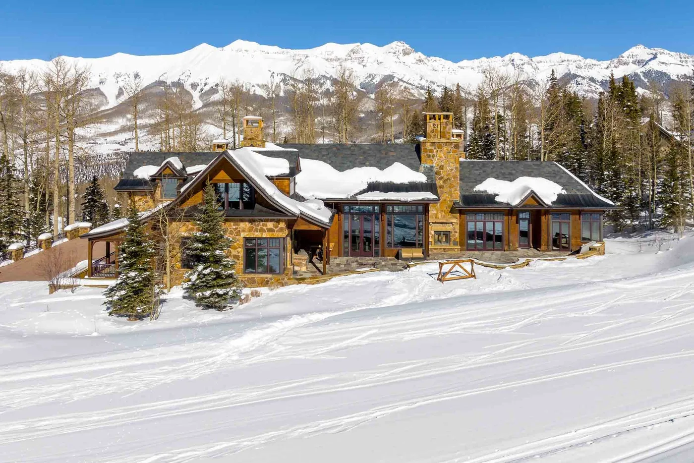 A mountain lodge stands beside a snow-covered slope beneath a clear blue sky.
