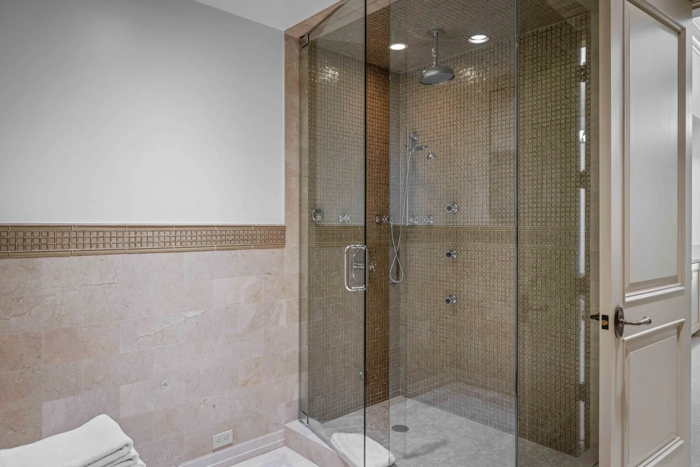 A tiled bathroom with a glass-enclosed shower and a white door.