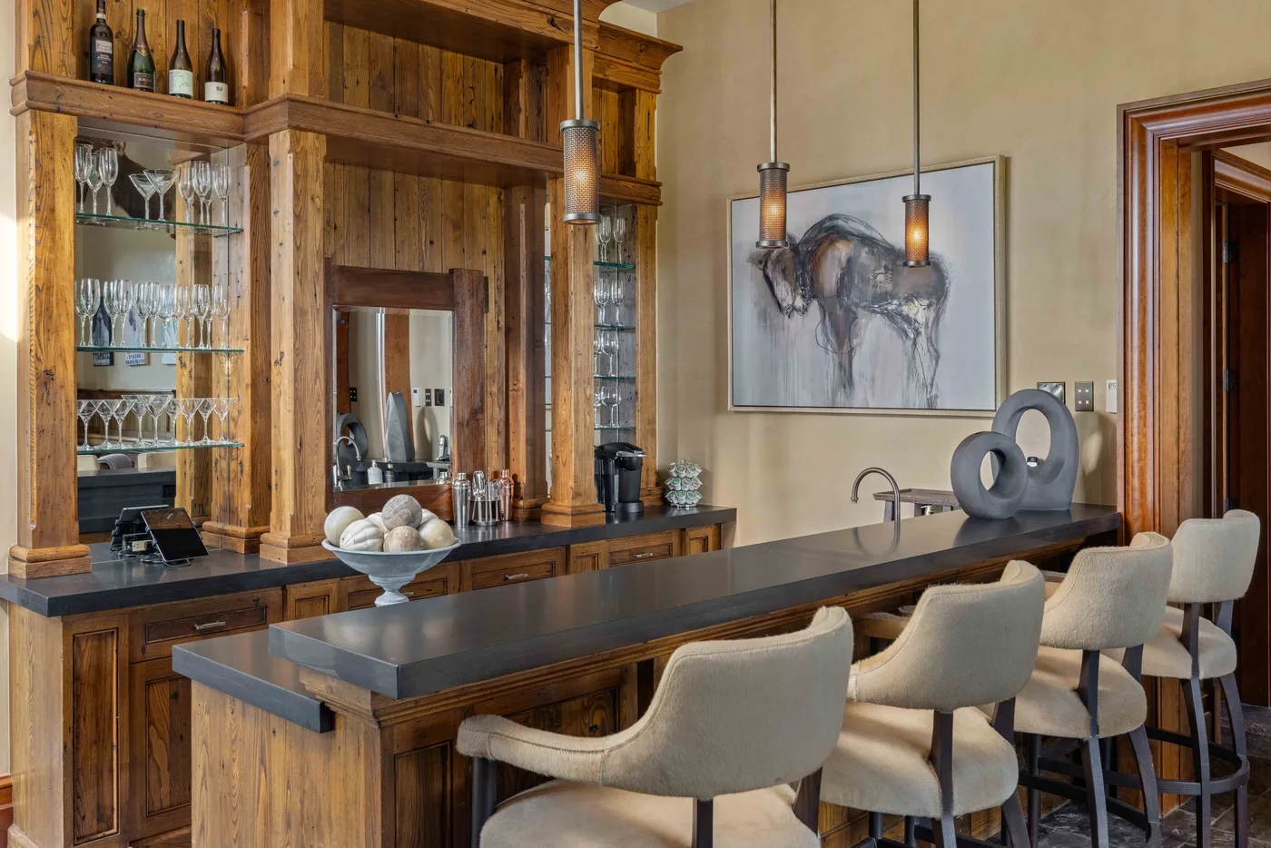 A wooden bar with stools sits beneath pendant lights beside built-in shelving.