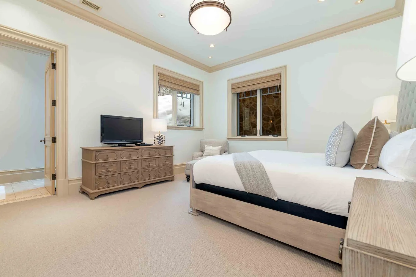 A bedroom with a neatly made bed, a dresser, and a television.