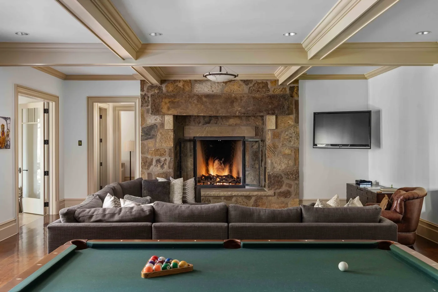 A living room with a stone fireplace, seating, and a pool table in the foreground.