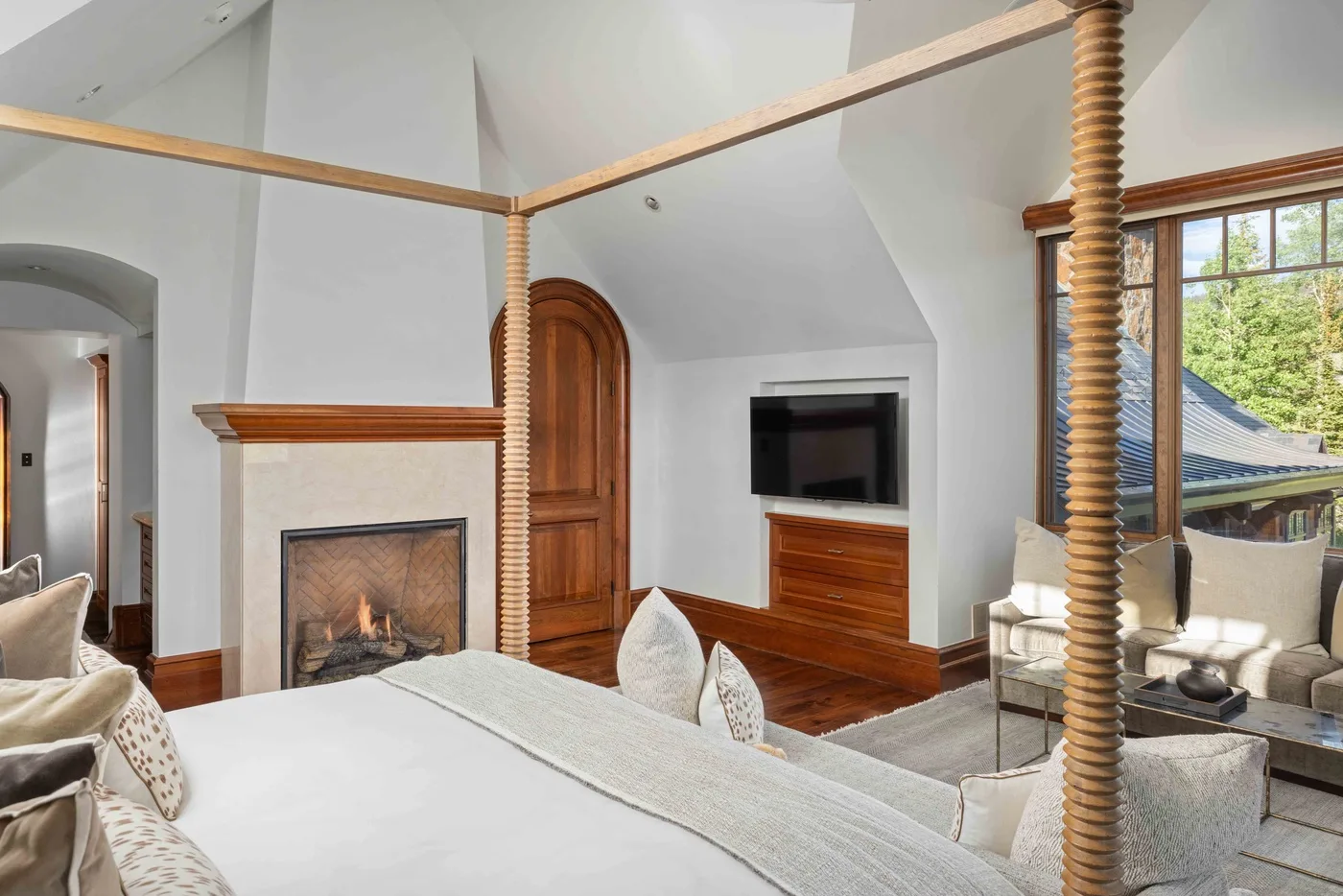 A bedroom with a fireplace, a four-poster bed, and a television.