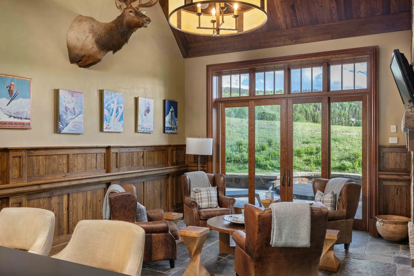 A wood-paneled sitting room with armchairs and large glass doors overlooking greenery.