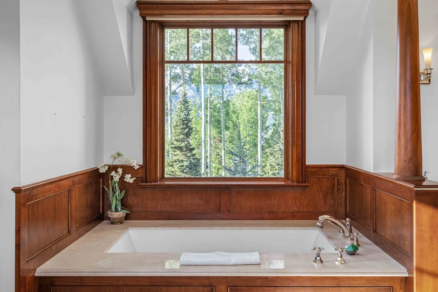 A built-in bathtub sits beneath a large window overlooking trees.
