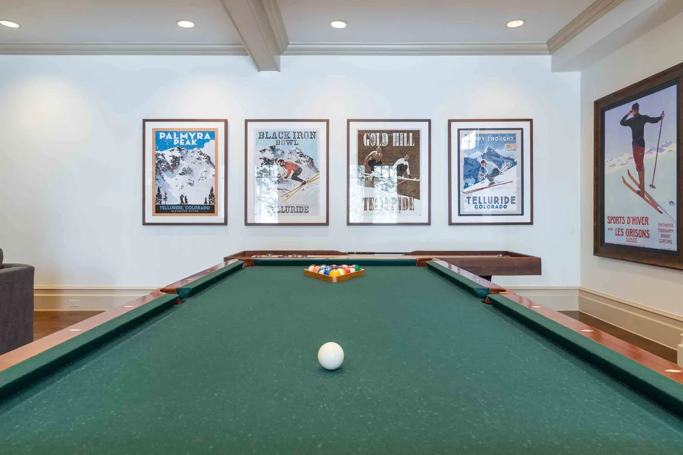 A billiards room with a green pool table and framed ski posters.