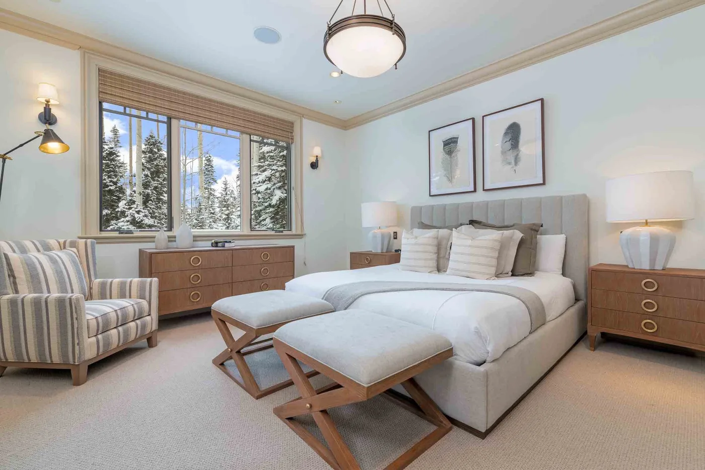 A bedroom with a large bed, upholstered benches, and a window overlooking trees.