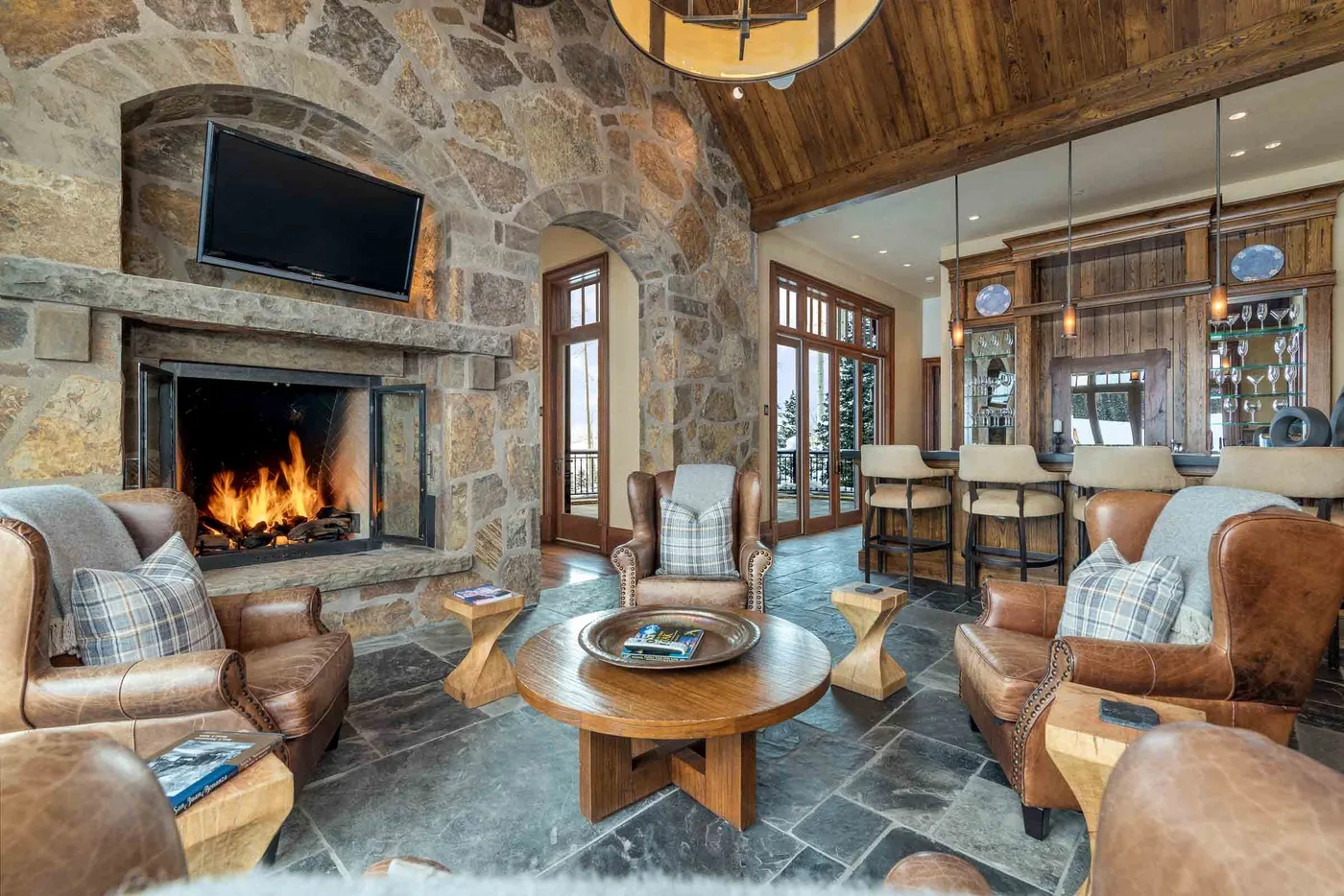 A rustic living room with a stone fireplace, seating, and an open kitchen.