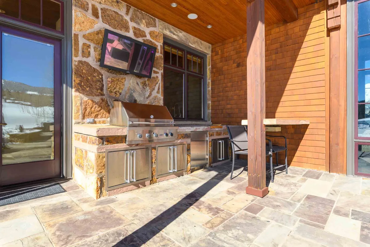 A covered outdoor kitchen and dining area with a stone counter and seating.