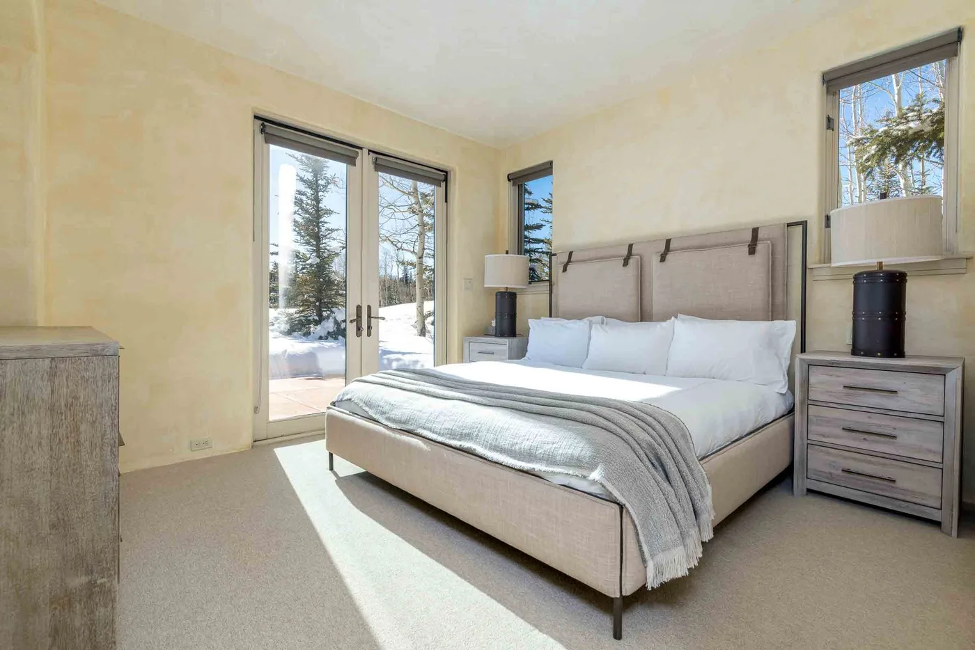 A bright bedroom with a bed, bedside tables, and glass doors opening to a patio.