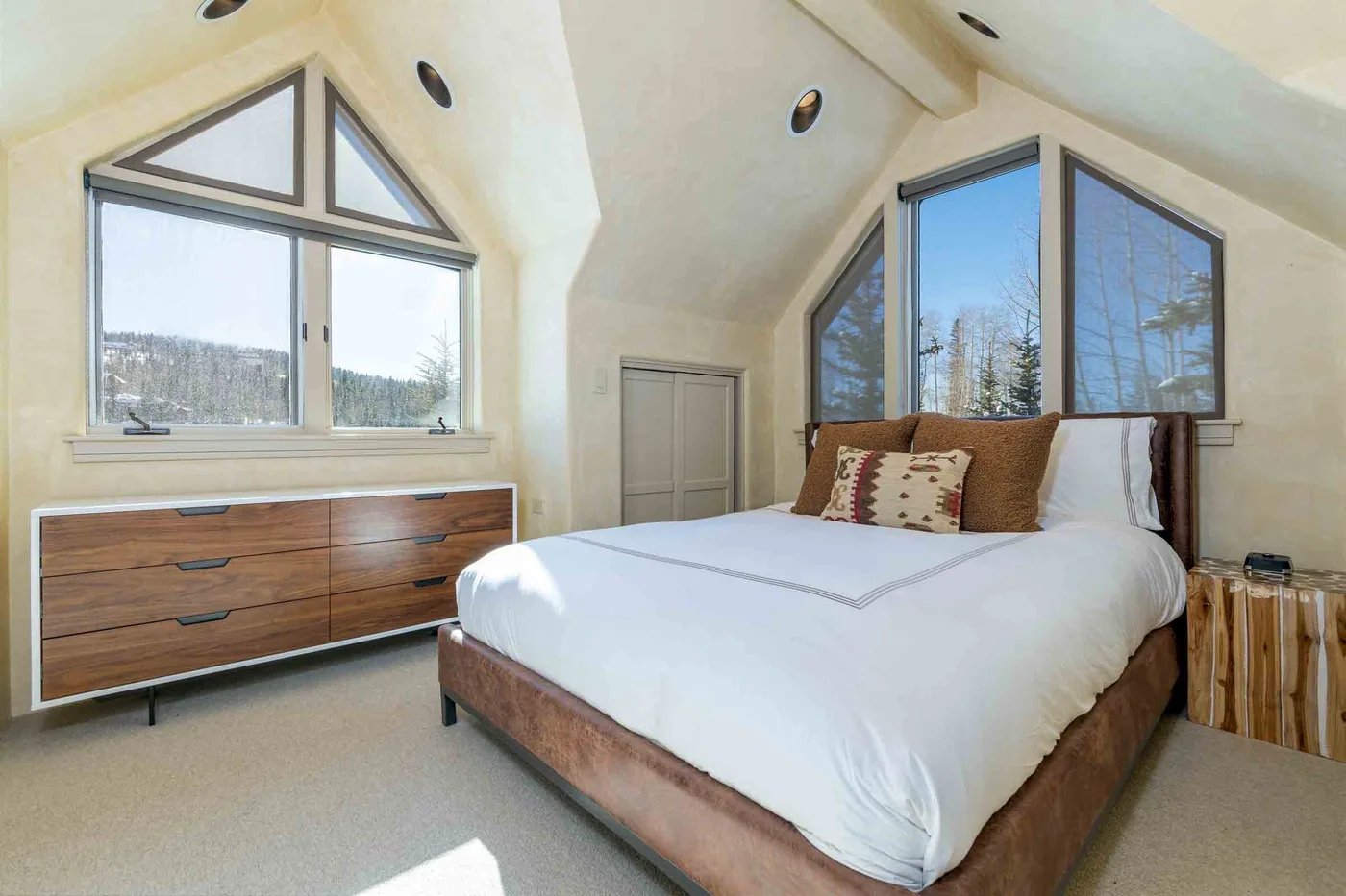 A bedroom with a bed beneath sloped ceilings and large windows.