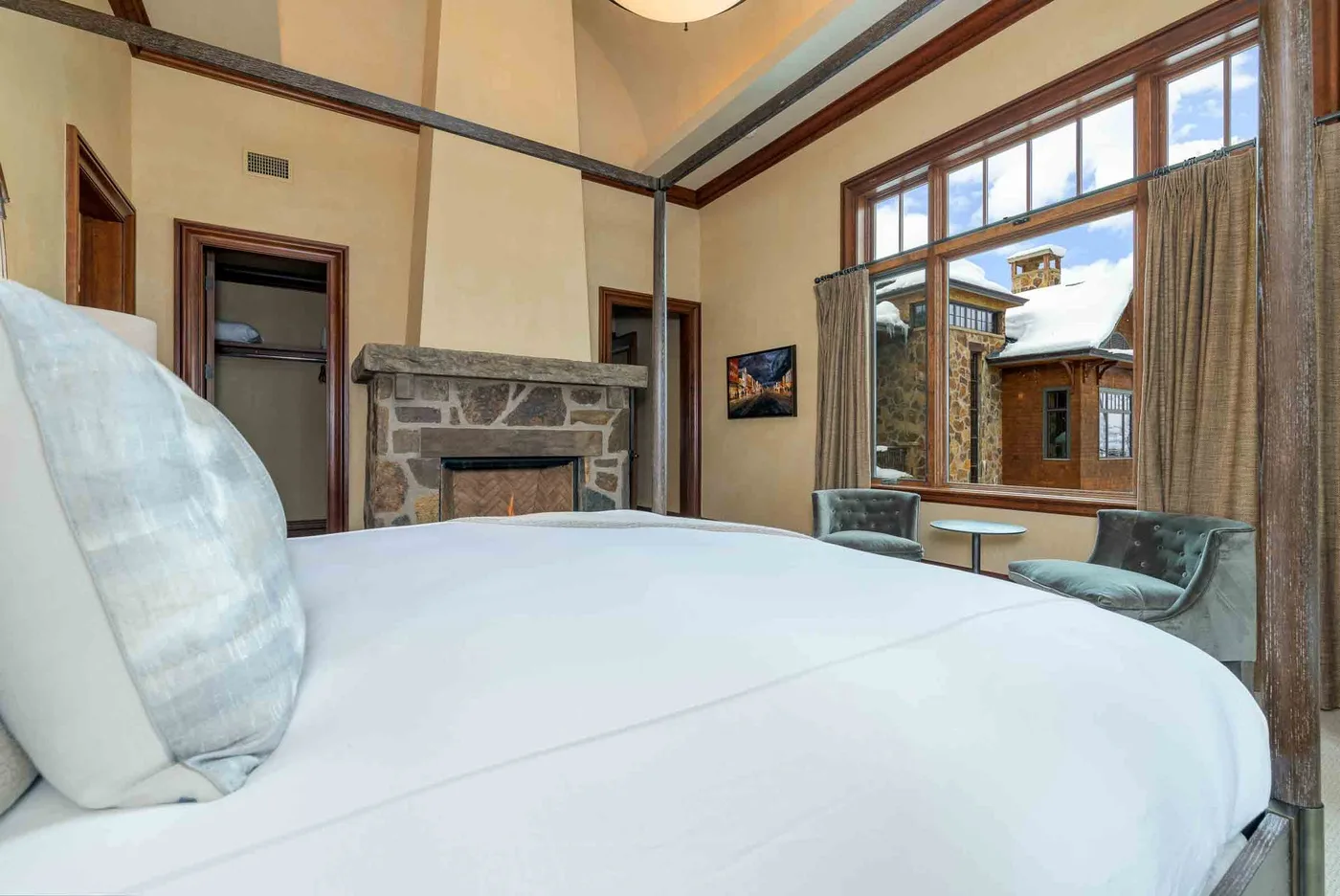 A bedroom with a large bed, stone fireplace, and seating beside tall windows.