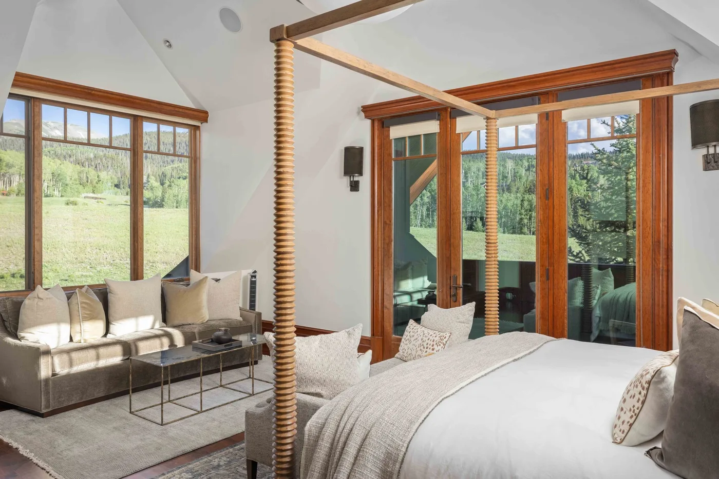 A bright bedroom with a bed and a seating area beside large windows.
