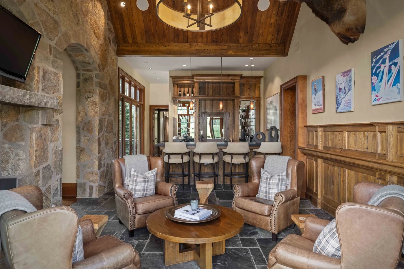 A rustic lounge with armchairs around a low wooden table and a bar area beyond.