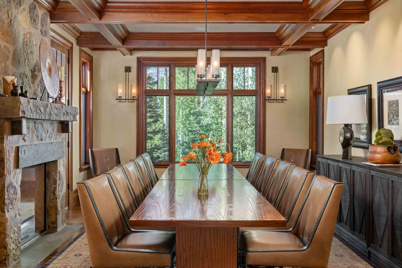 A dining room with a long table, upholstered seating, and large windows.