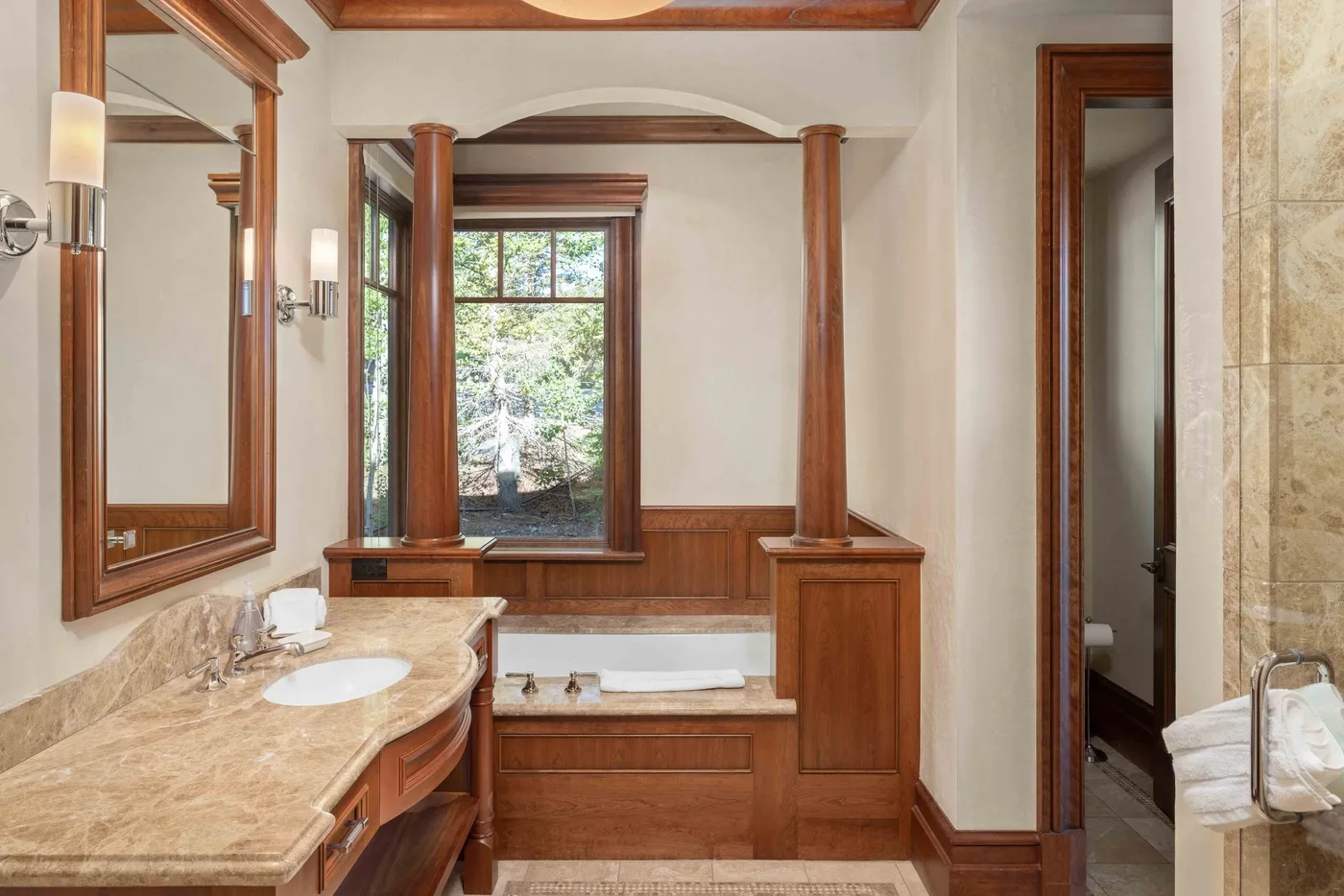 A bathroom with a long stone vanity and a soaking tub beneath a window.
