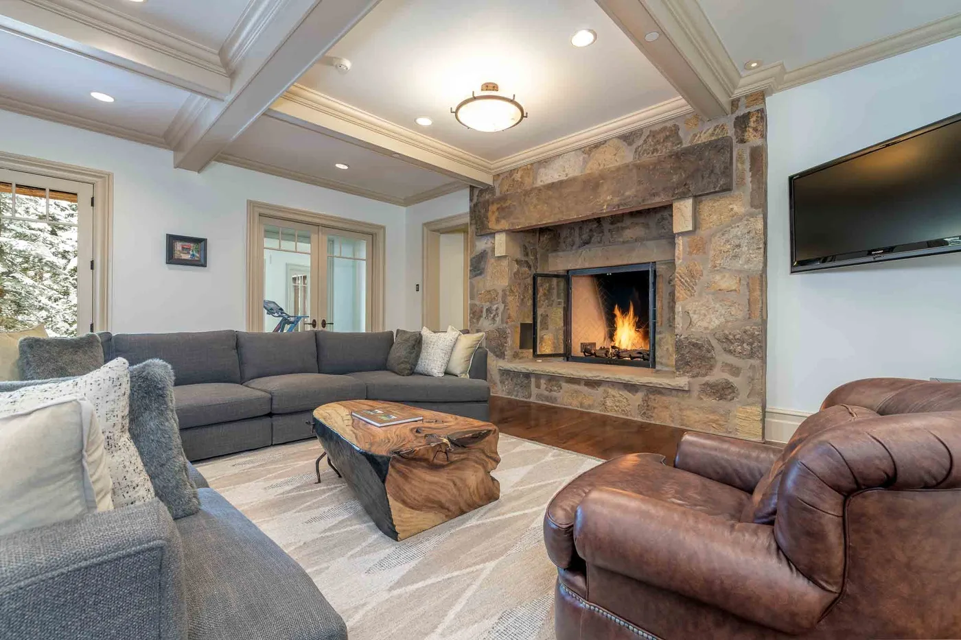 A living room with a stone fireplace, sectional seating, and a wall-mounted television.