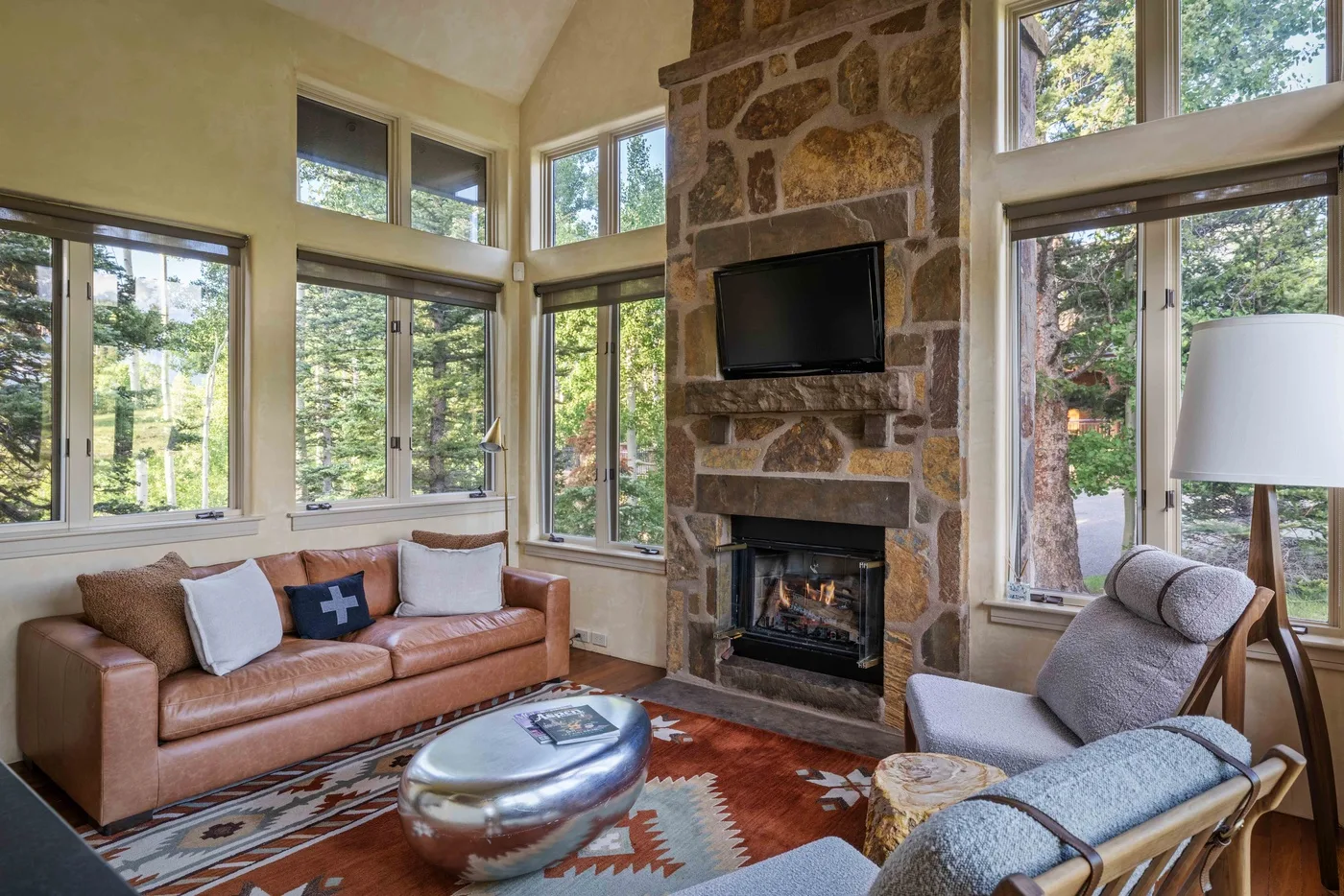 A living room with large windows, a stone fireplace, and seating around a coffee table.