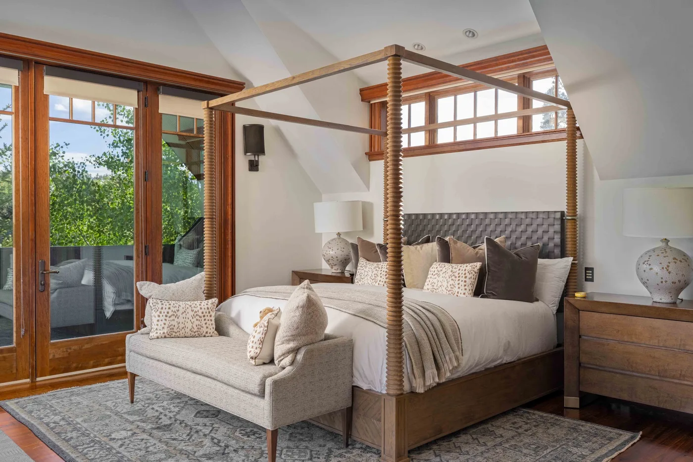 A bedroom with a four-poster bed, upholstered seating, and large windows.