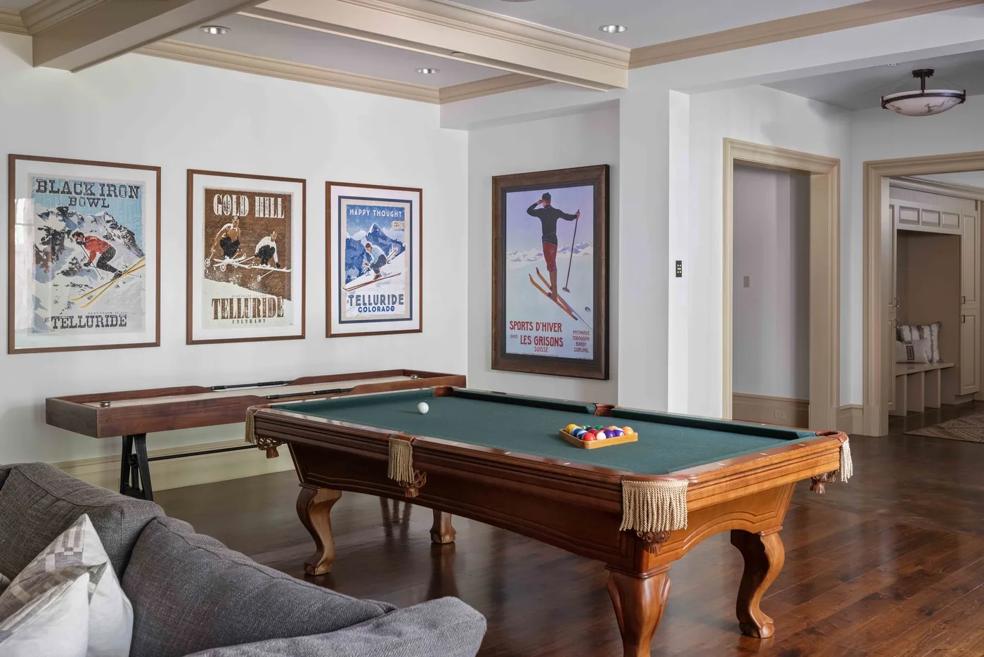 A billiards room with a green-felt pool table and framed ski posters.