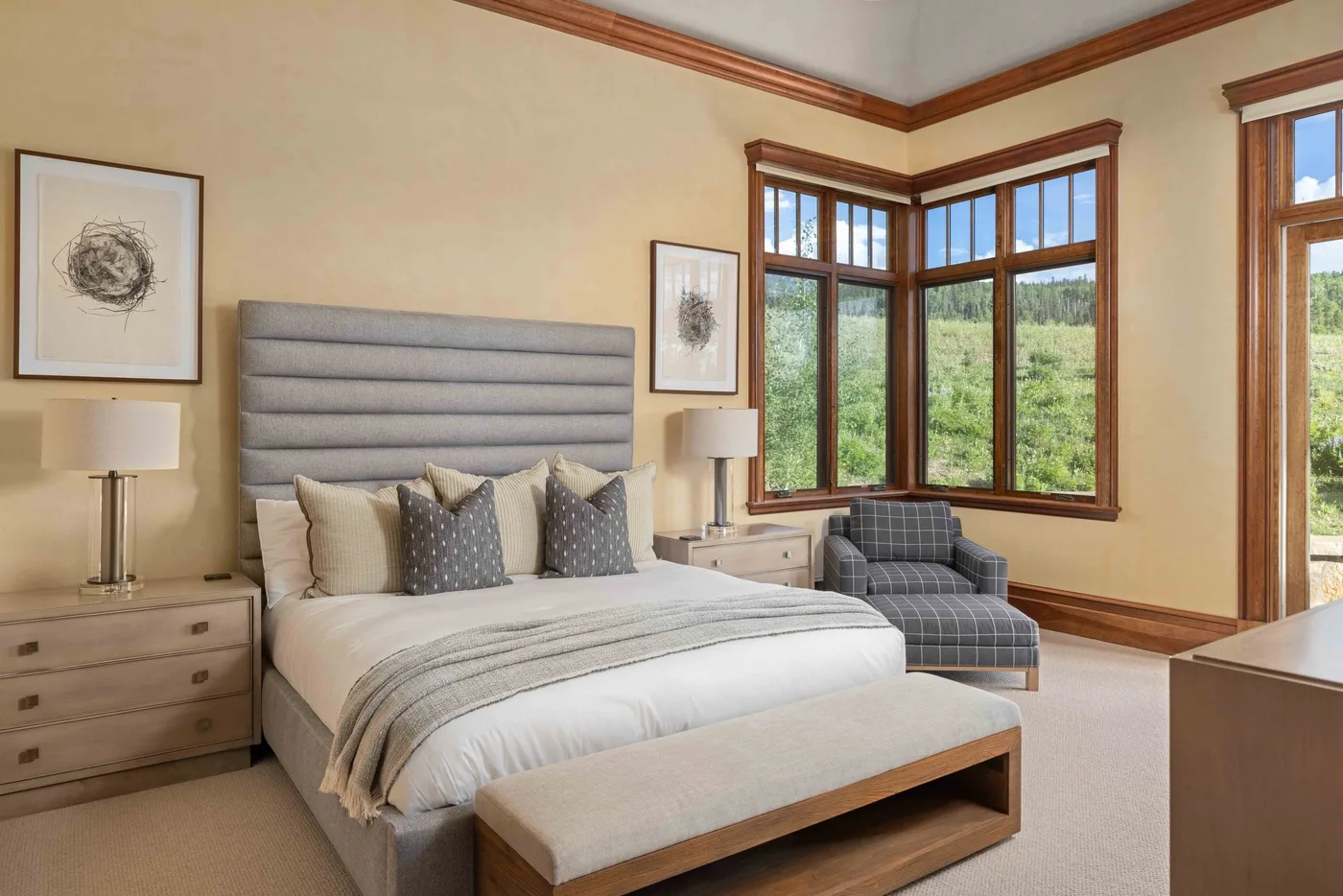 A bedroom with a neatly made bed and large windows overlooking greenery.