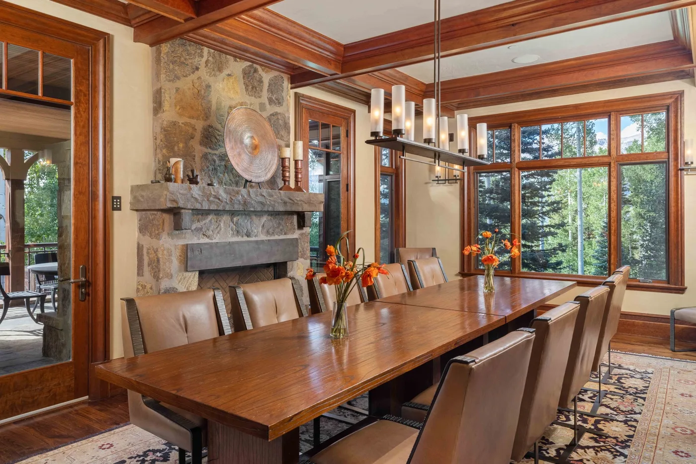 A dining room with a long wooden table, seating, and a stone fireplace.