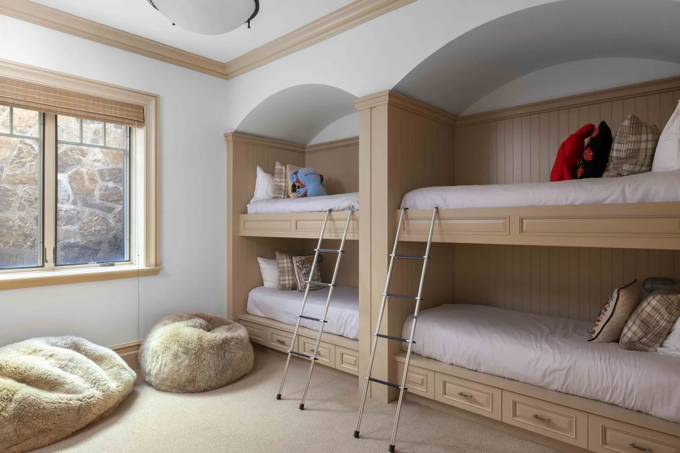 A bedroom with built-in bunk beds, ladders, and a window.