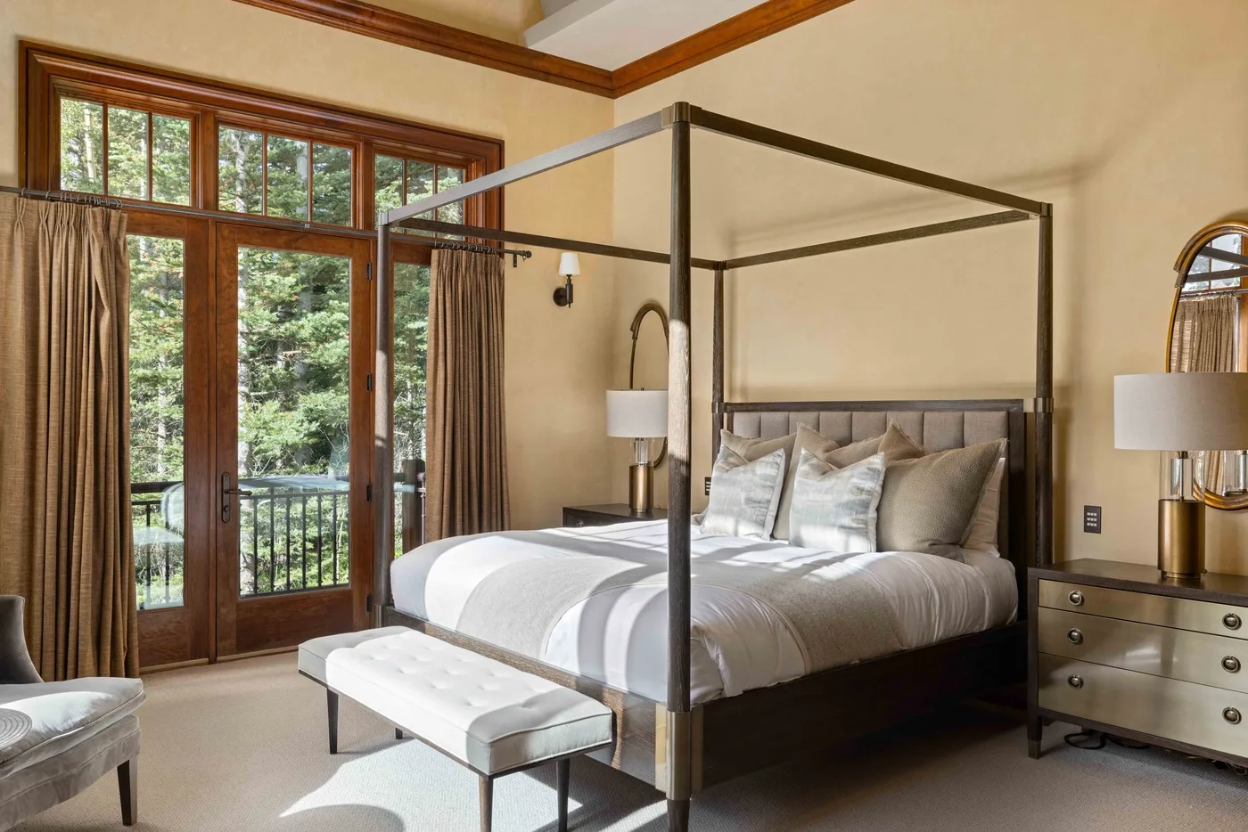 A bright bedroom with a canopy bed and tall windows overlooking greenery.