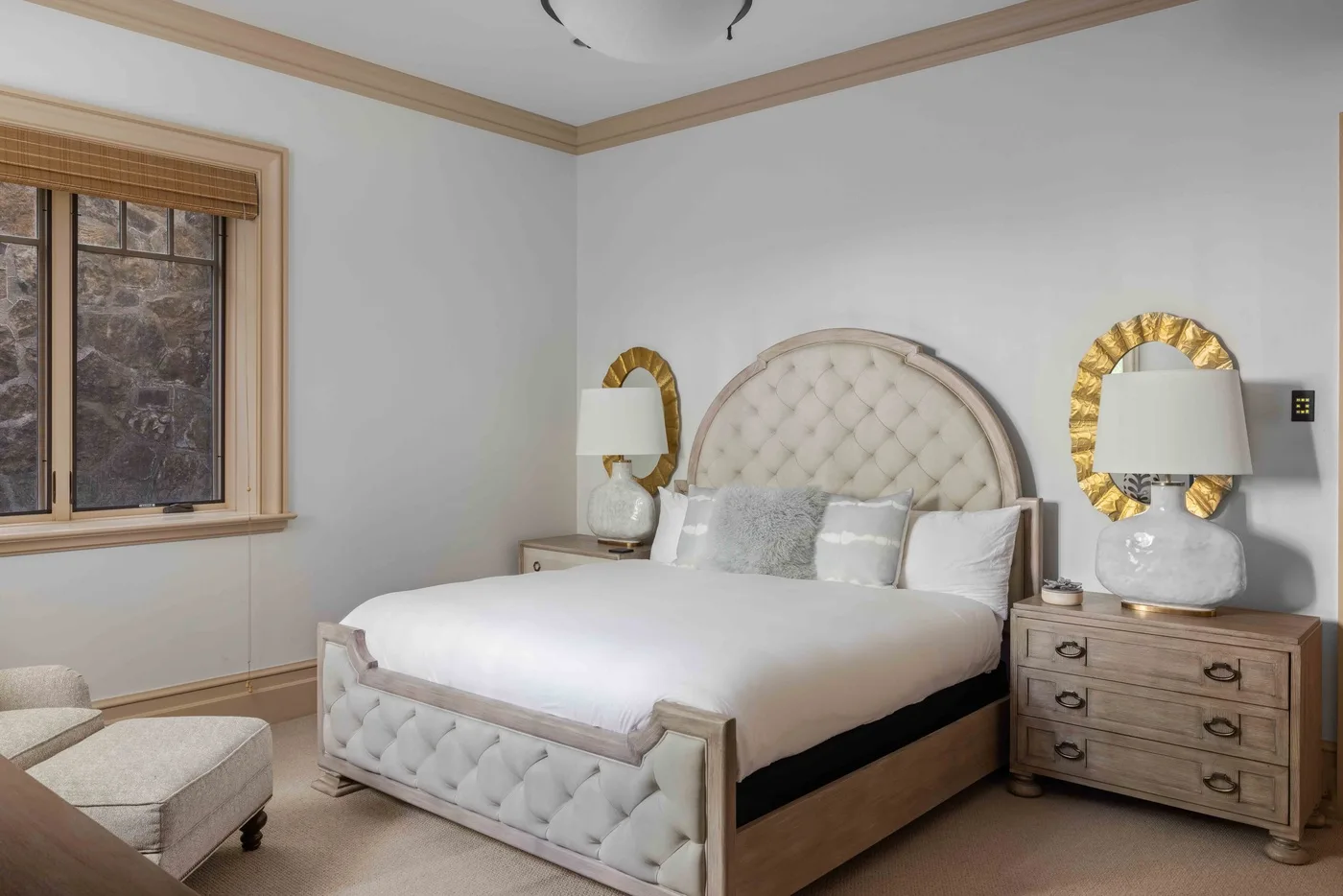 A bedroom with a tufted bed, bedside lamps, and a window.