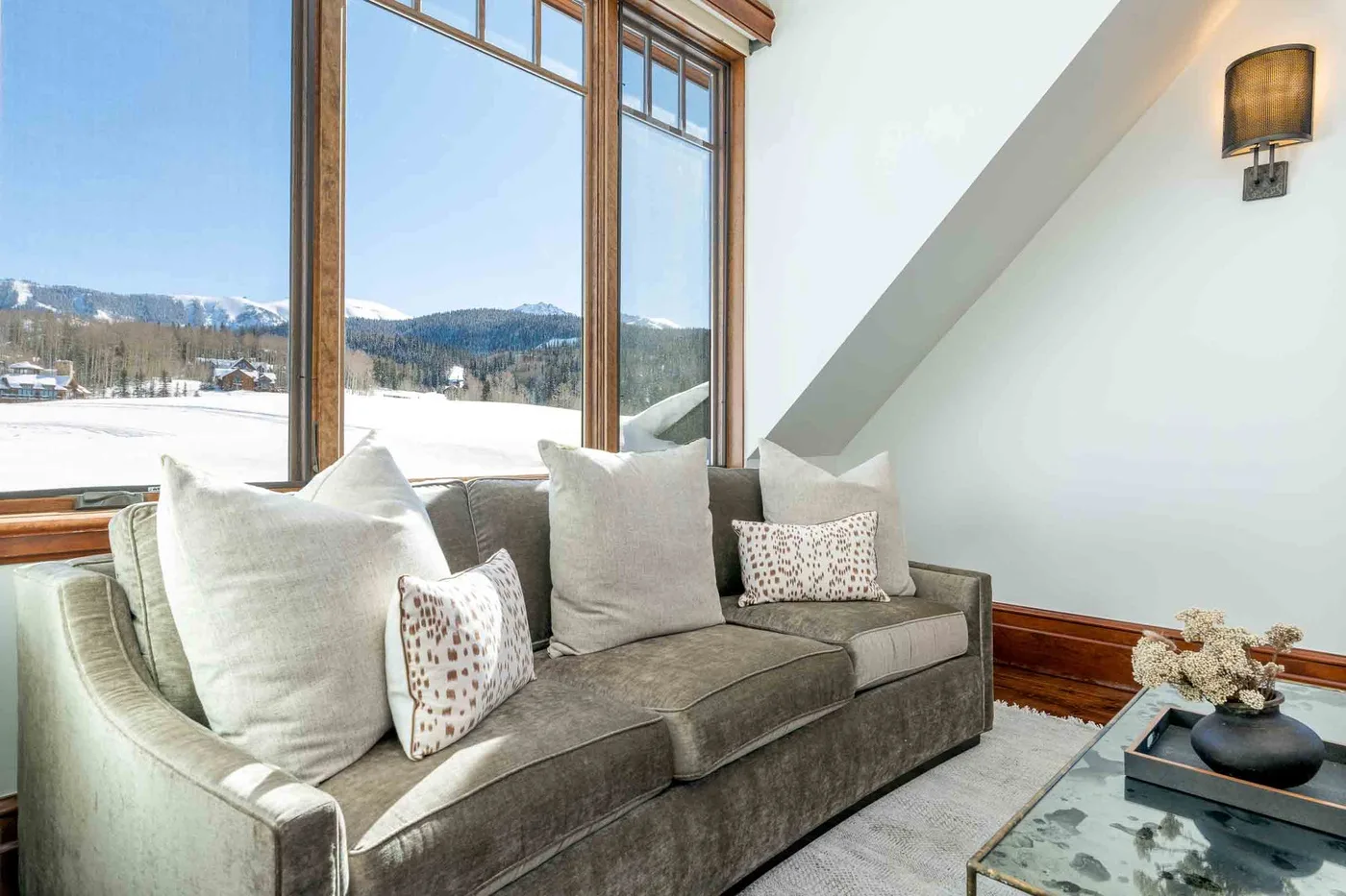 A living room with a gray sofa beside large windows overlooking a snowy landscape.