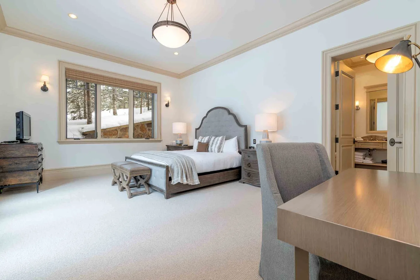 A bright bedroom with a large window, a bed, and a desk.