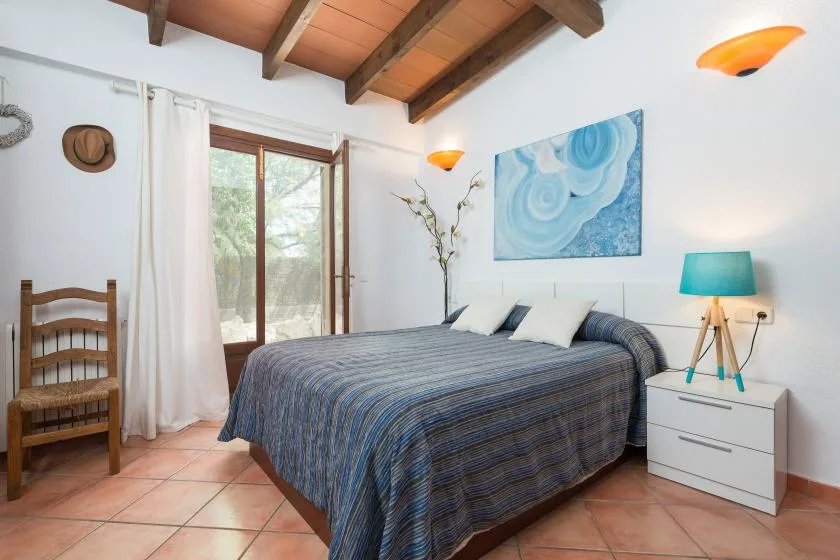 A bedroom with a double bed, a wooden chair, and a window.