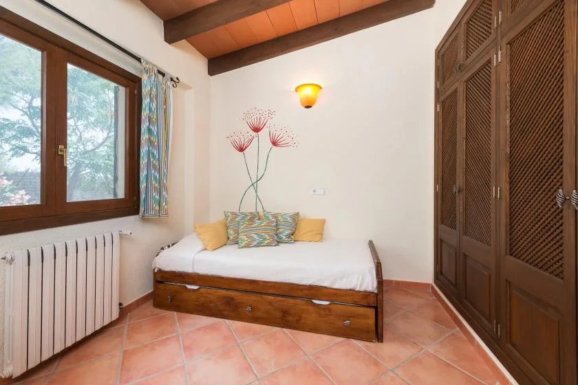 A bedroom with a low bed, a window, and tall wooden wardrobes.