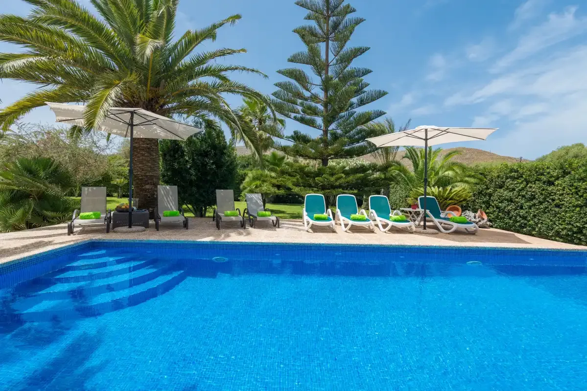An outdoor swimming pool is surrounded by lounge seating, parasols, and palm trees.
