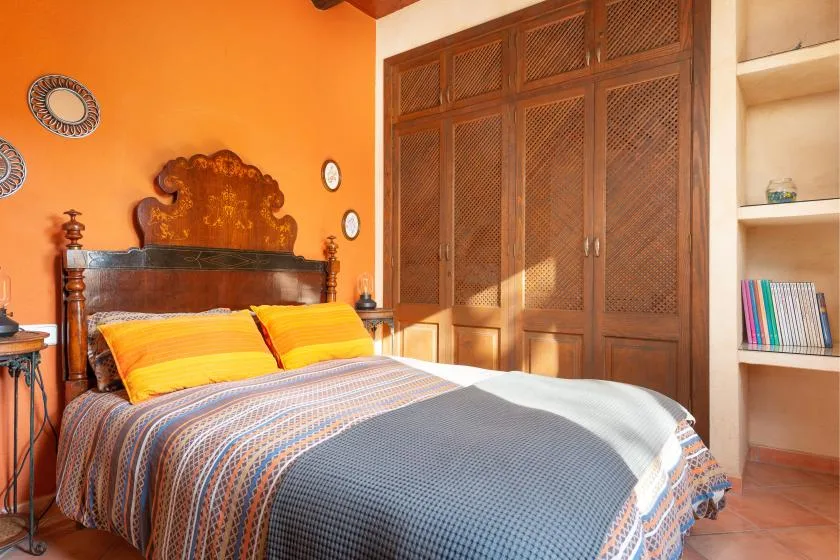 A bedroom with a bed, colorful bedding, and a large wooden wardrobe.