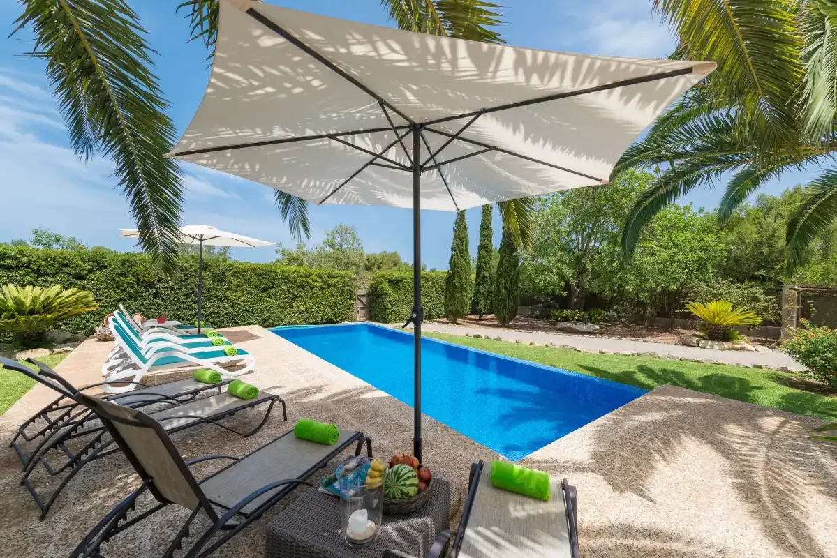 An outdoor swimming pool is surrounded by lounge seating and greenery.