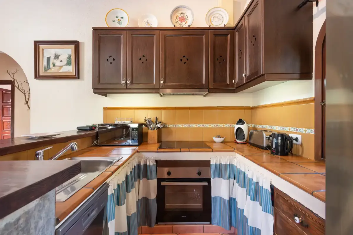 A kitchen with dark wooden cabinets, tiled counters, and cooking appliances.