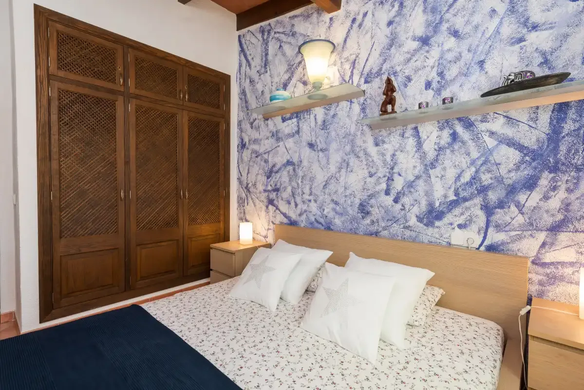 A bedroom with a bed, wooden wardrobe, and blue patterned wall.