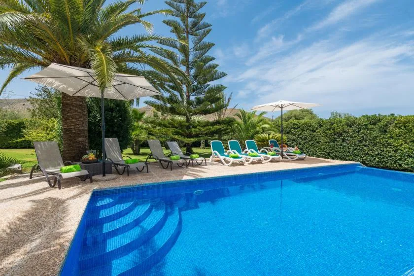 An outdoor swimming pool is bordered by lounge seating and greenery.